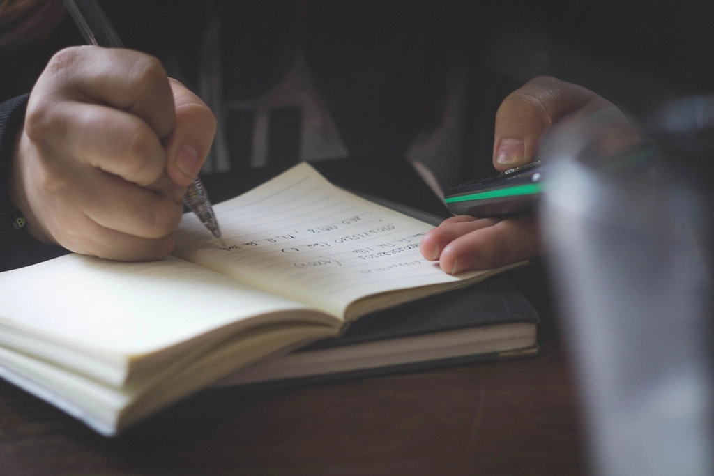 Manos escribiendo en una libreta con luz tenue